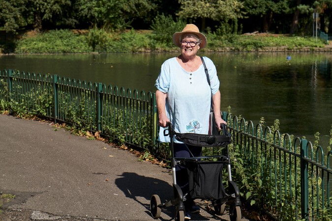 IMAGE 3 Photograph showing a woman in a sunhat walking in a park using a mobility aid for assistance.