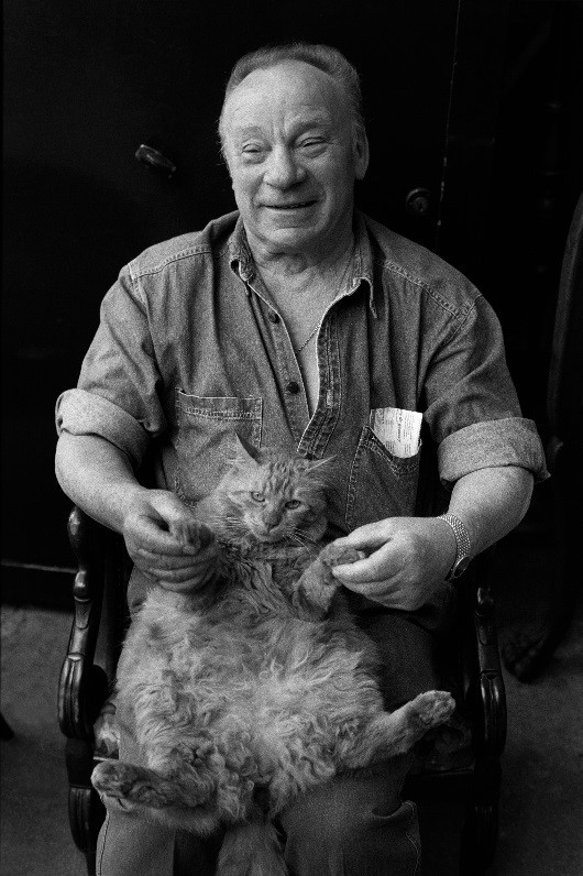 Black and white picture of older man holding cat on his lap.