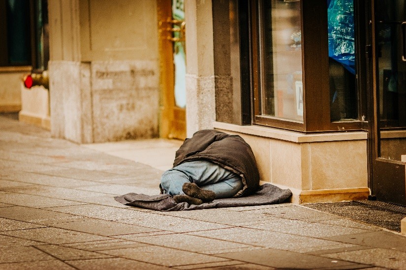 IMAGE 1: Photograph showing a person sleeping rough on a blanket outside a shop front.